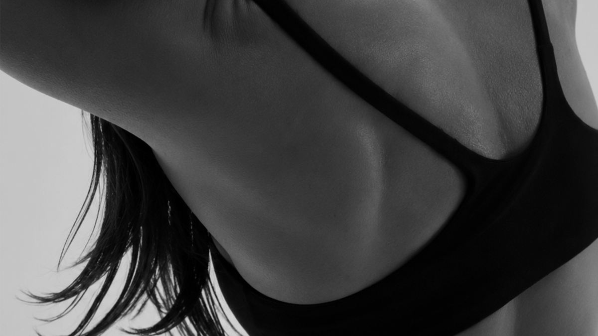 Black-and-white close view of a woman's upper back and shoulder blade in a sports bra, head turned away