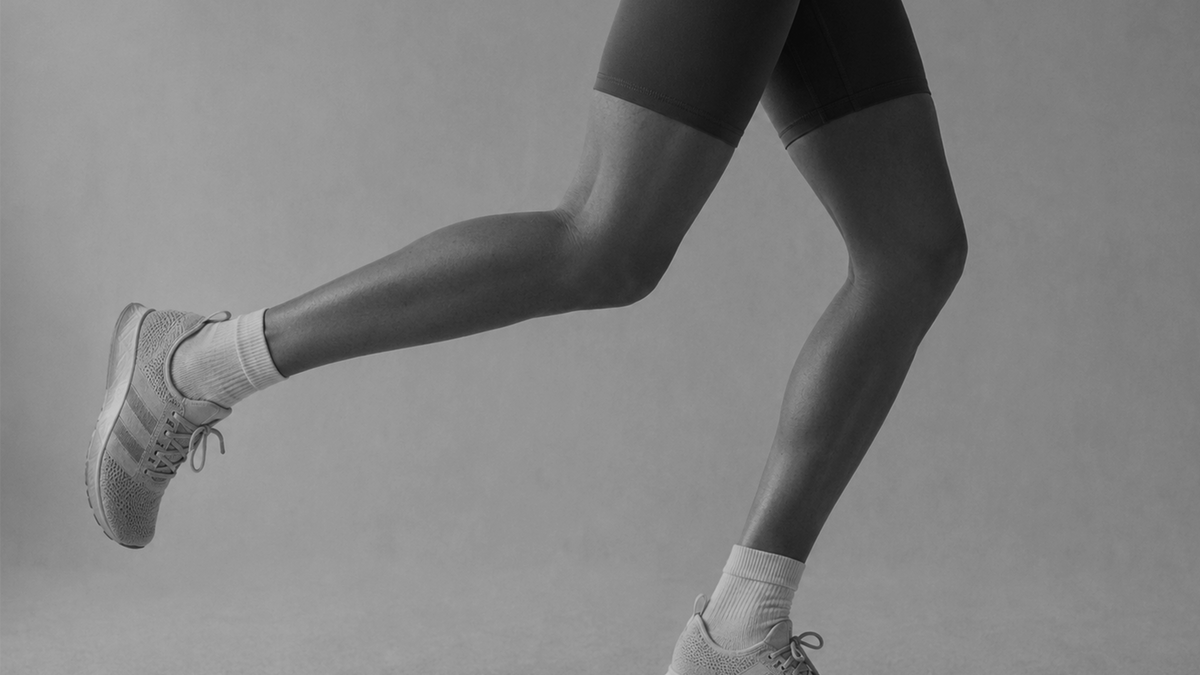 Black-and-white side view of a runner's legs mid-stride in dark shorts and white sneakers against a grey backdrop